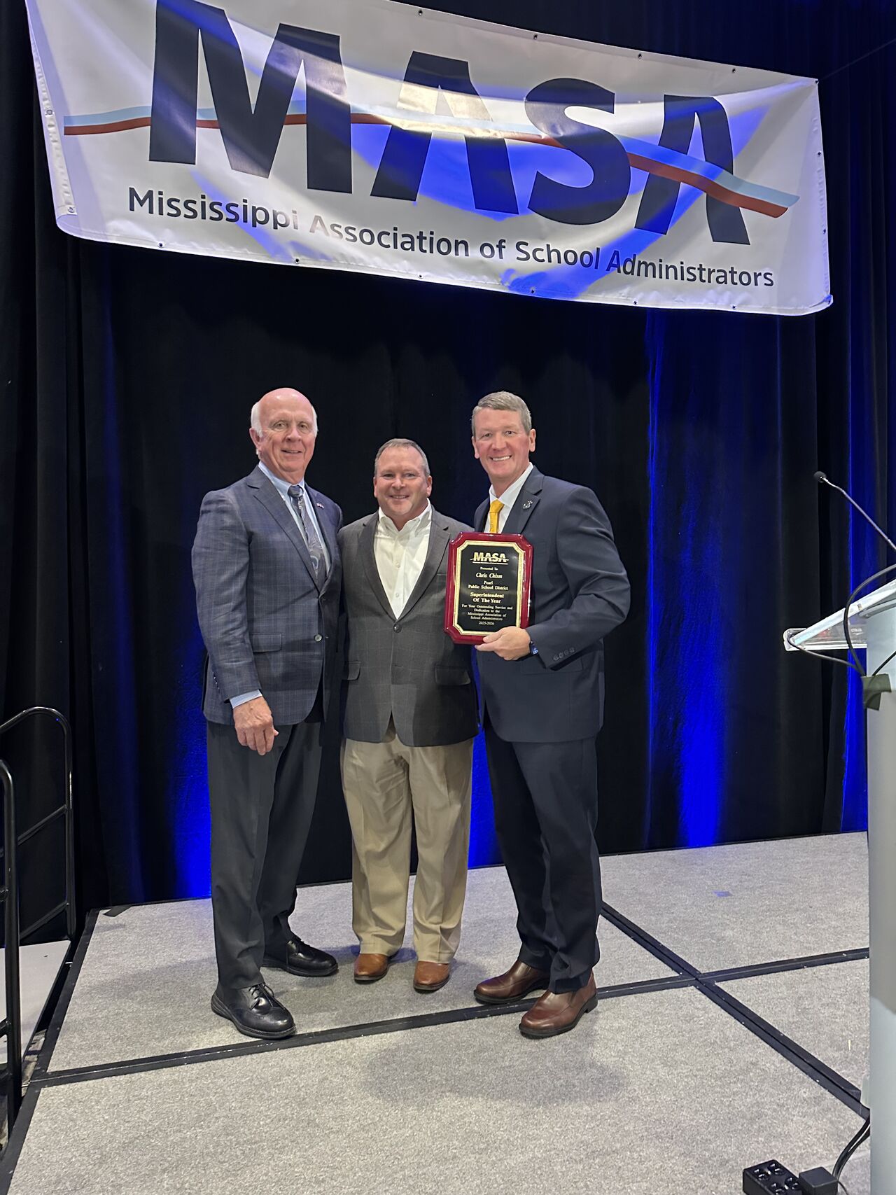 Chris Chism receiving the Mississippi Superintendent of the Year plaque on stage from MASA