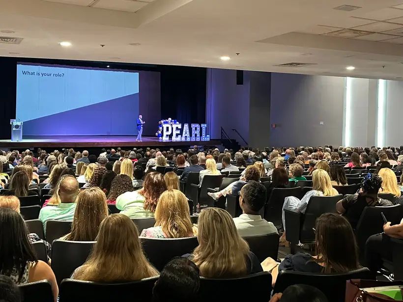 Chris Chism on stage delivering a keynote address to hundreds of Pearl Public School District staff, PEARL marquee letters visible behind him